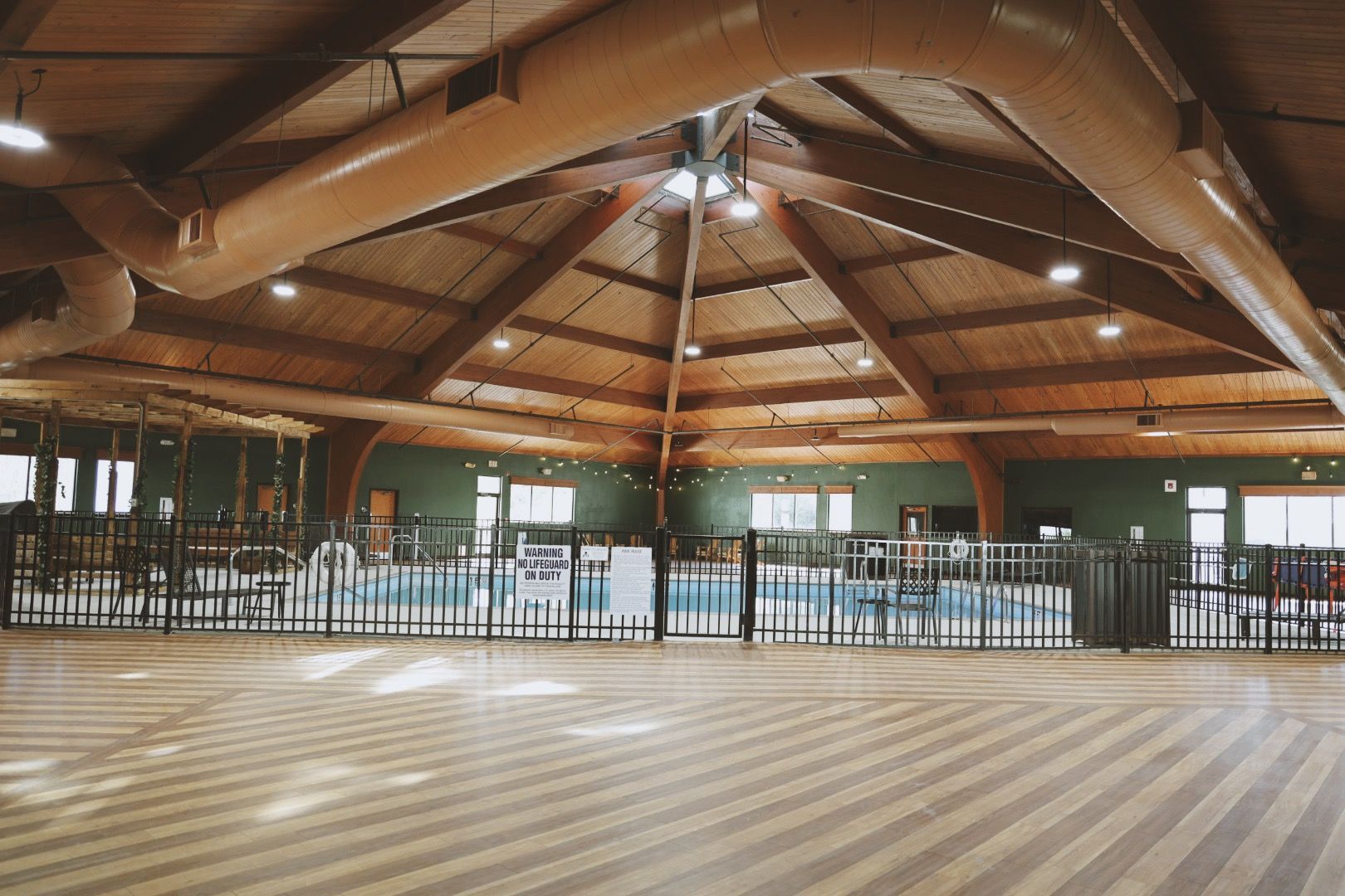 A large room with a wooden floor and a swimming pool in the background.