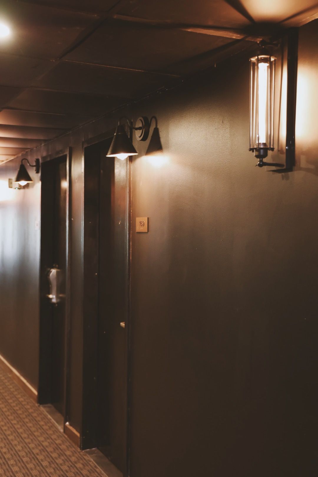 A hallway with a lot of doors and lights on the wall.
