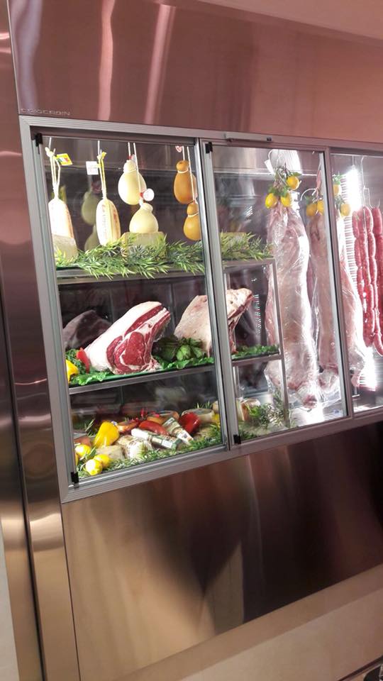 Vetrina per la carne: vari tagli di carne cruda, formaggi e salsicce esposti in un espositore refrigerato.