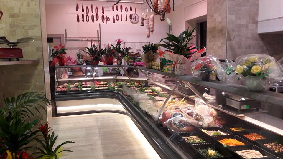 Interno di una macelleria con una lunga vetrina piena di cibo e carni appese.