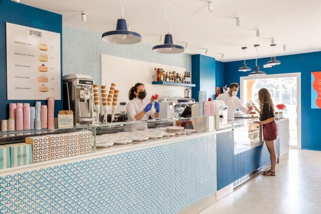 L'interno di una gelateria: pareti blu, bancone con i dolci, personale che serve un cliente.