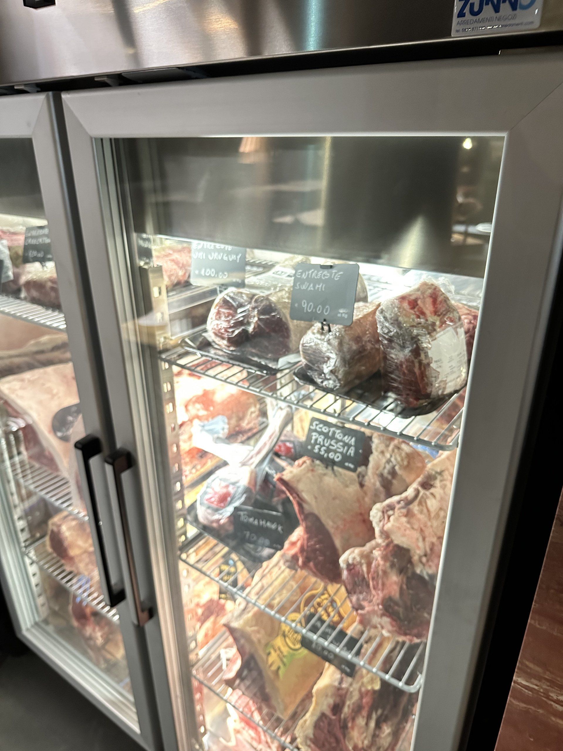 Vetrina frigorifera che espone vari tagli di carne cruda, probabilmente in vendita in una macelleria o in un ristorante.