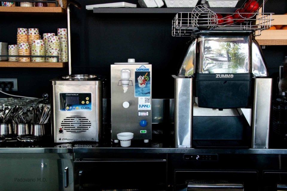 Bancone della caffetteria con tre macchine per bevande, tazze e utensili.