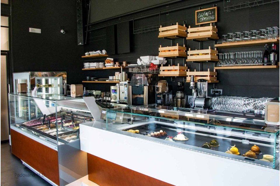 Interno di una gelateria con vetrine in vetro, dettagli in legno e pareti nere.