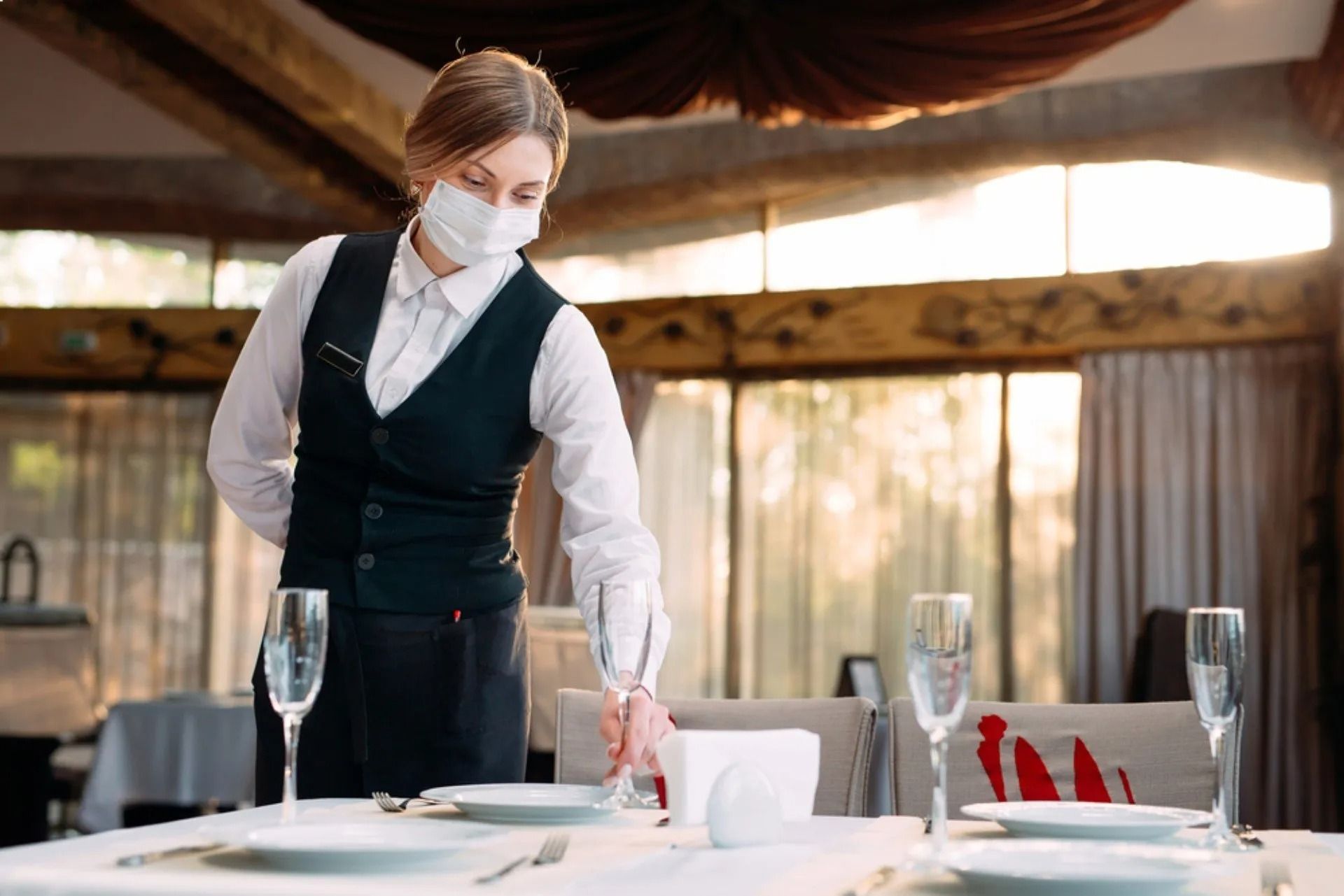 Il cameriere con la mascherina apparecchia il tavolo in un ristorante.