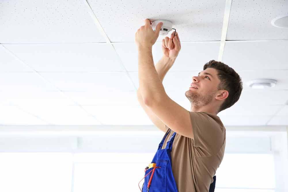 Young Electrician Installing Smoke Detector on Ceiling — Level 2 Electrician in Toukley, NSW
