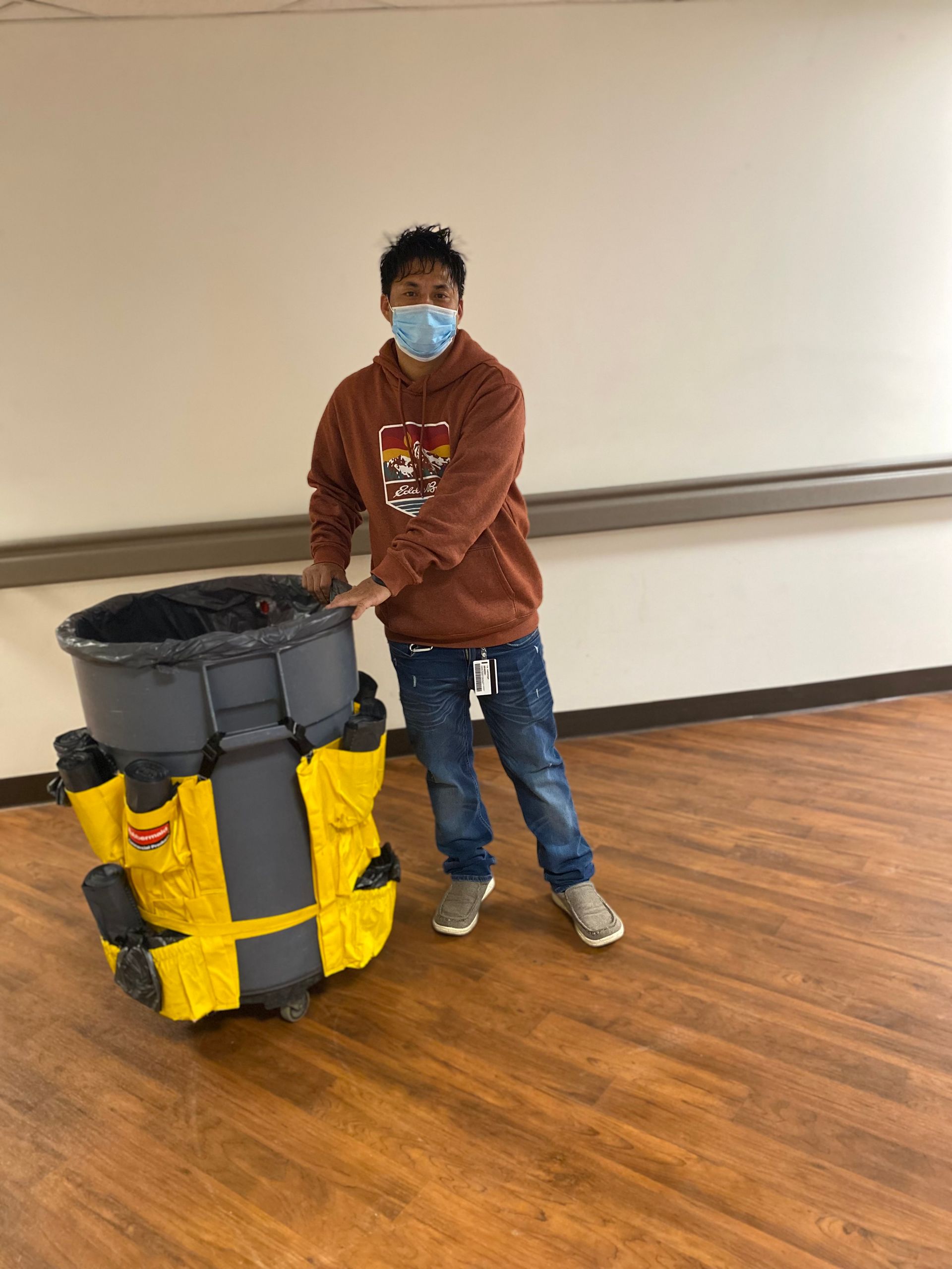 A man wearing a mask is standing next to a large trash can.