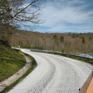 Curving gravel road through wooded hills under a partly cloudy sky