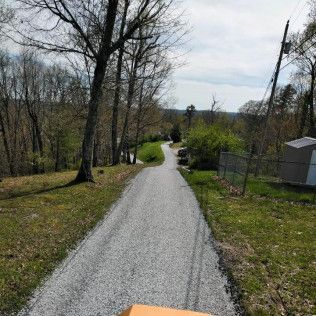 Gravel path winding through a wooded area with leafless trees and a fence on the right.