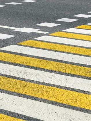 Yellow-and-white zebra crossing on a gray asphalt road, viewed at an angle.