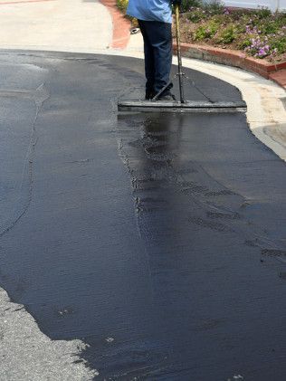 Person smoothing fresh black asphalt with a long-handled tool on a driveway edge.
