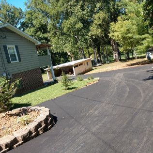 Curved black driveway beside a house and trees in a wooded residential area