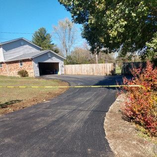 Freshly paved driveway leading to a brick house with garage, blocked by yellow caution tape