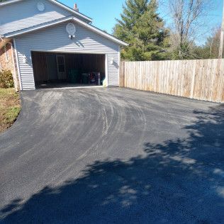 Driveway leading to an open garage beside a wooden fence on a sunny day