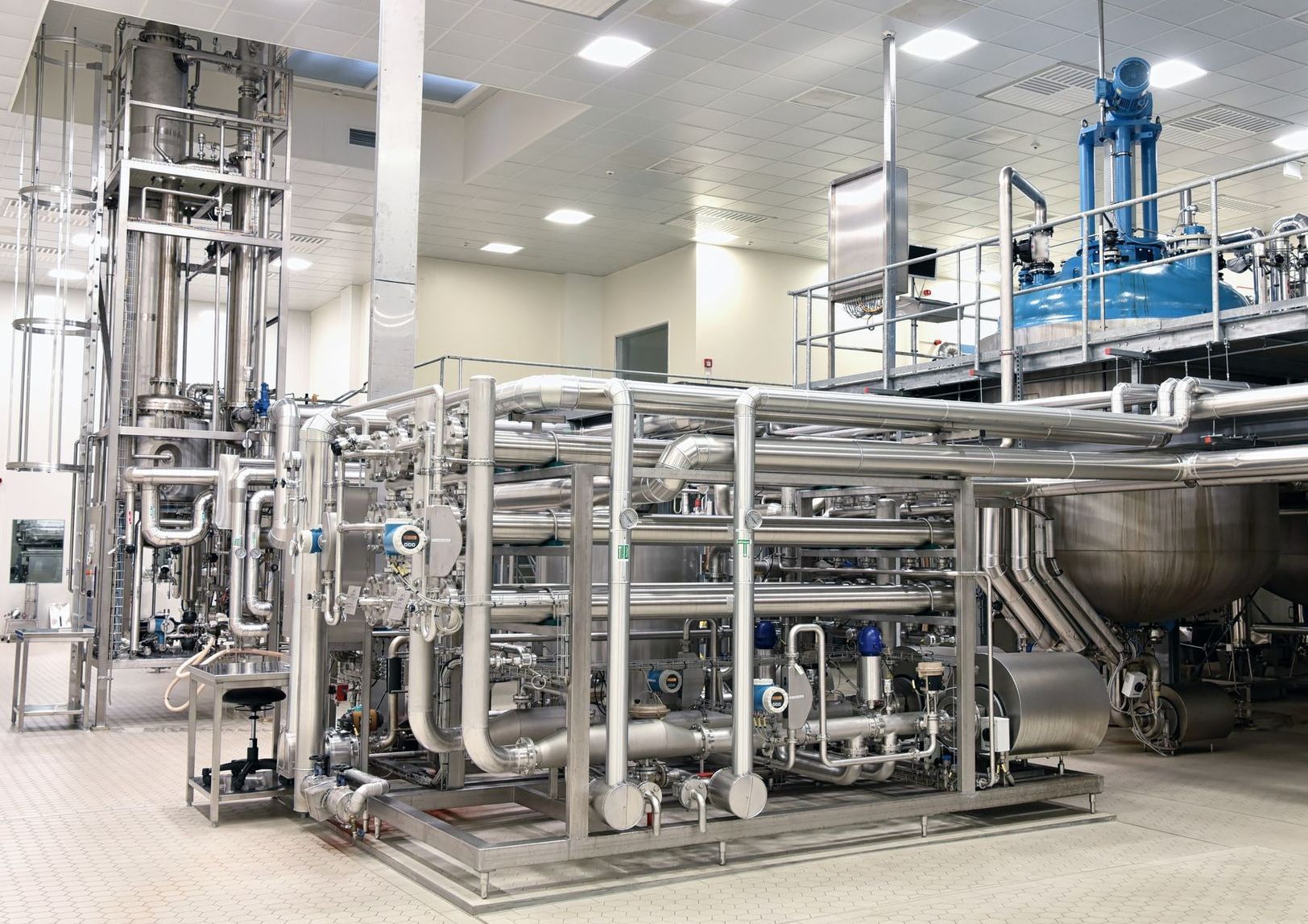 Industrial stainless-steel processing equipment in a clean factory room with pipes, tanks, and valves