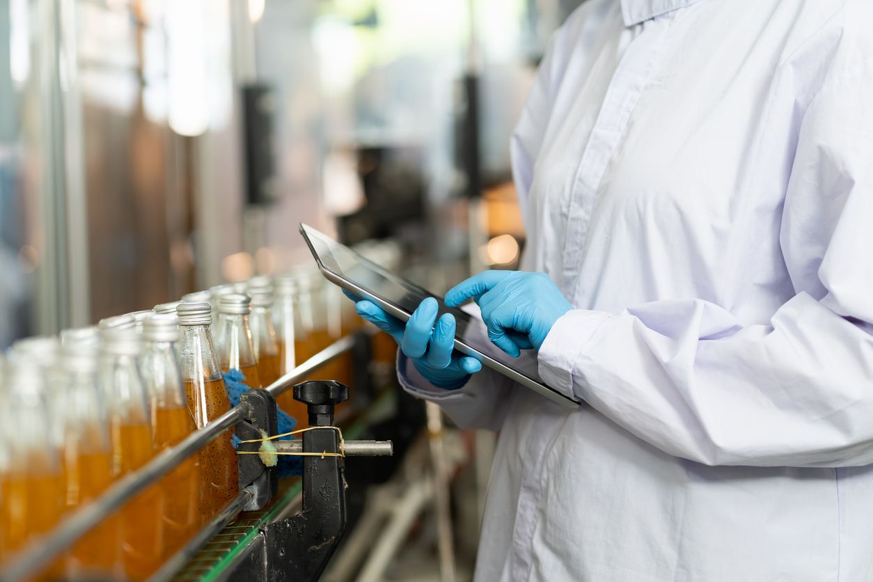 Lab technician in gloves inspecting bottles on a conveyor line with a tablet
