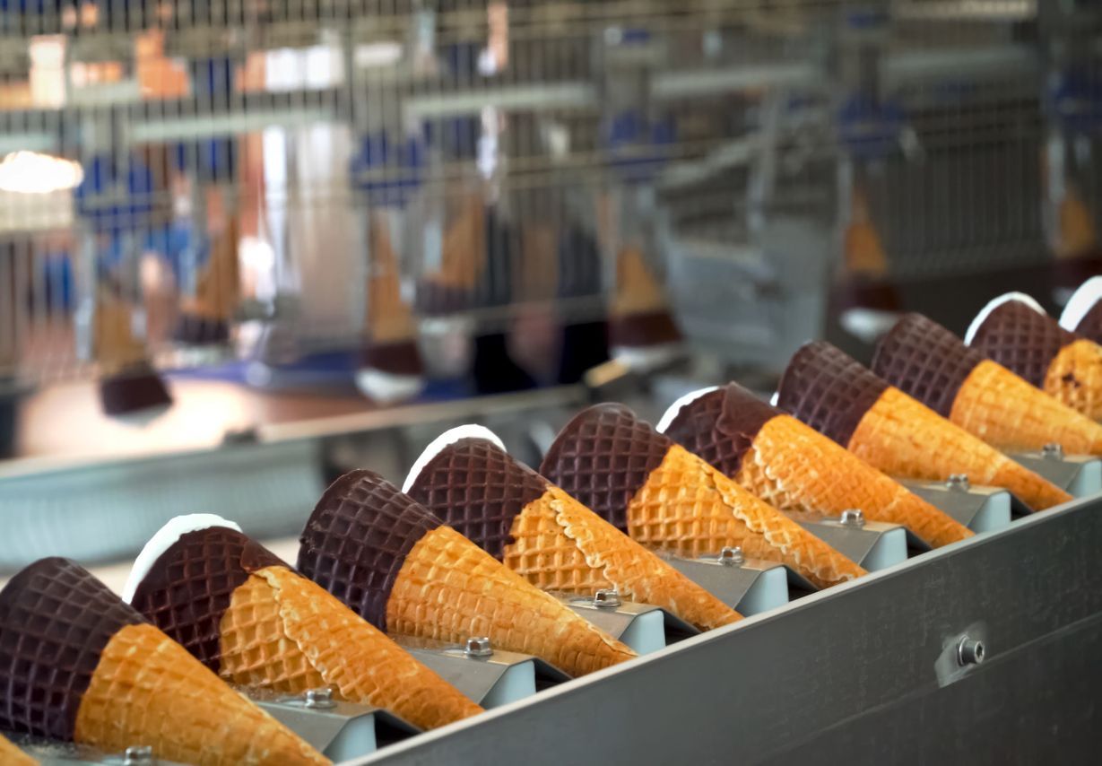 Ice cream cones with chocolate tops moving along a metal factory production line.