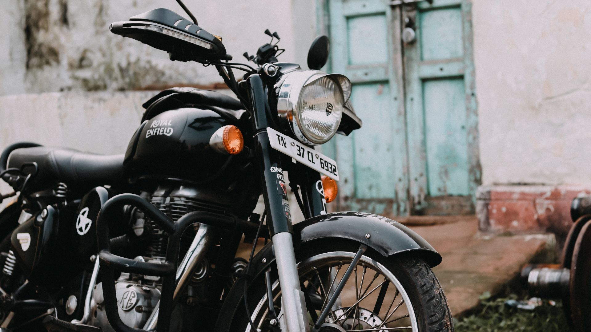 Black motorcycle parked by a weathered wall and blue door on a damp street