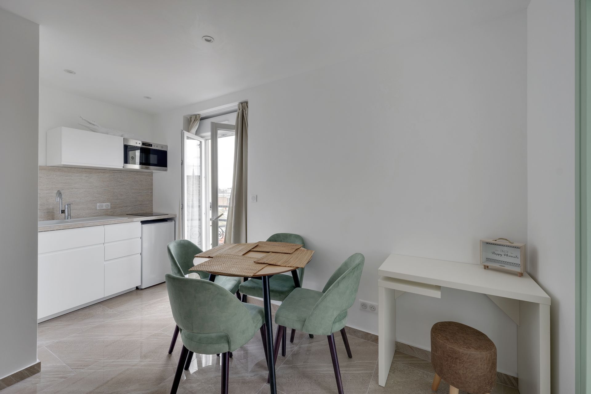 Small apartment interior with a kitchen, dining table, and desk. White and green color scheme.