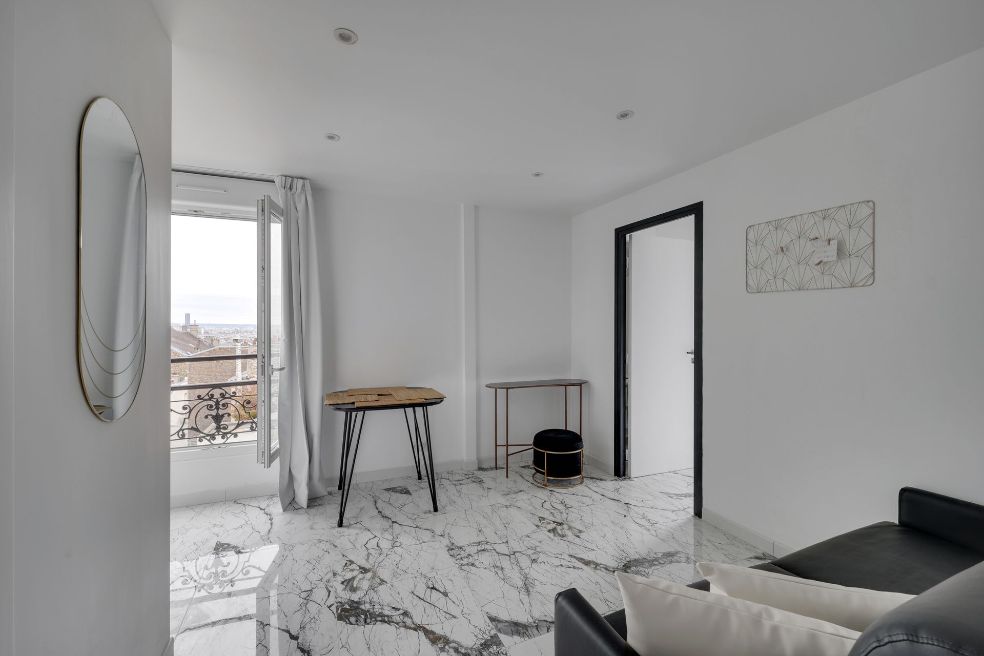 Bright white room with marble floors, small table, and balcony overlooking a cityscape.