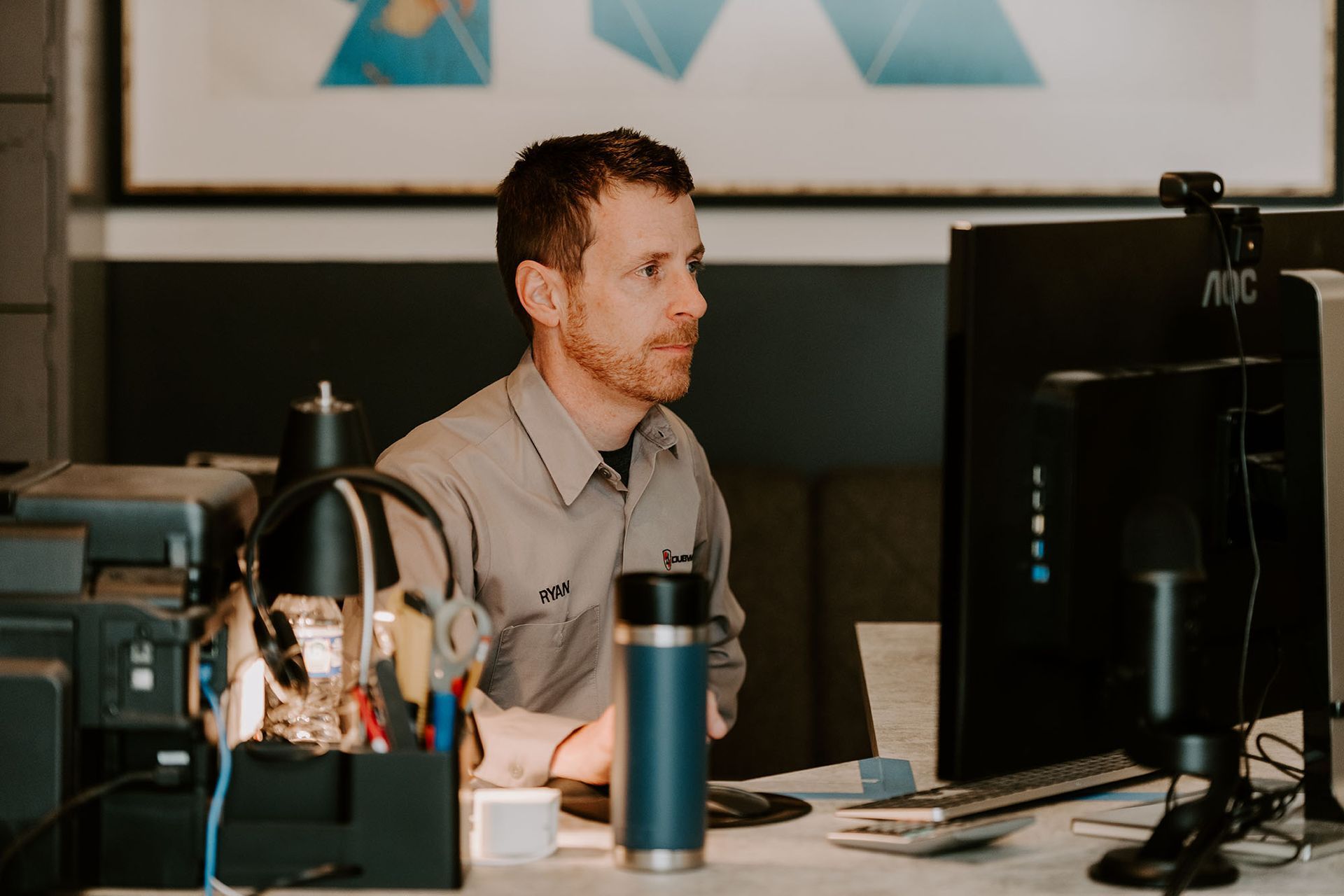 Man working at a desk with computer monitors and office equipment in a modern workspace