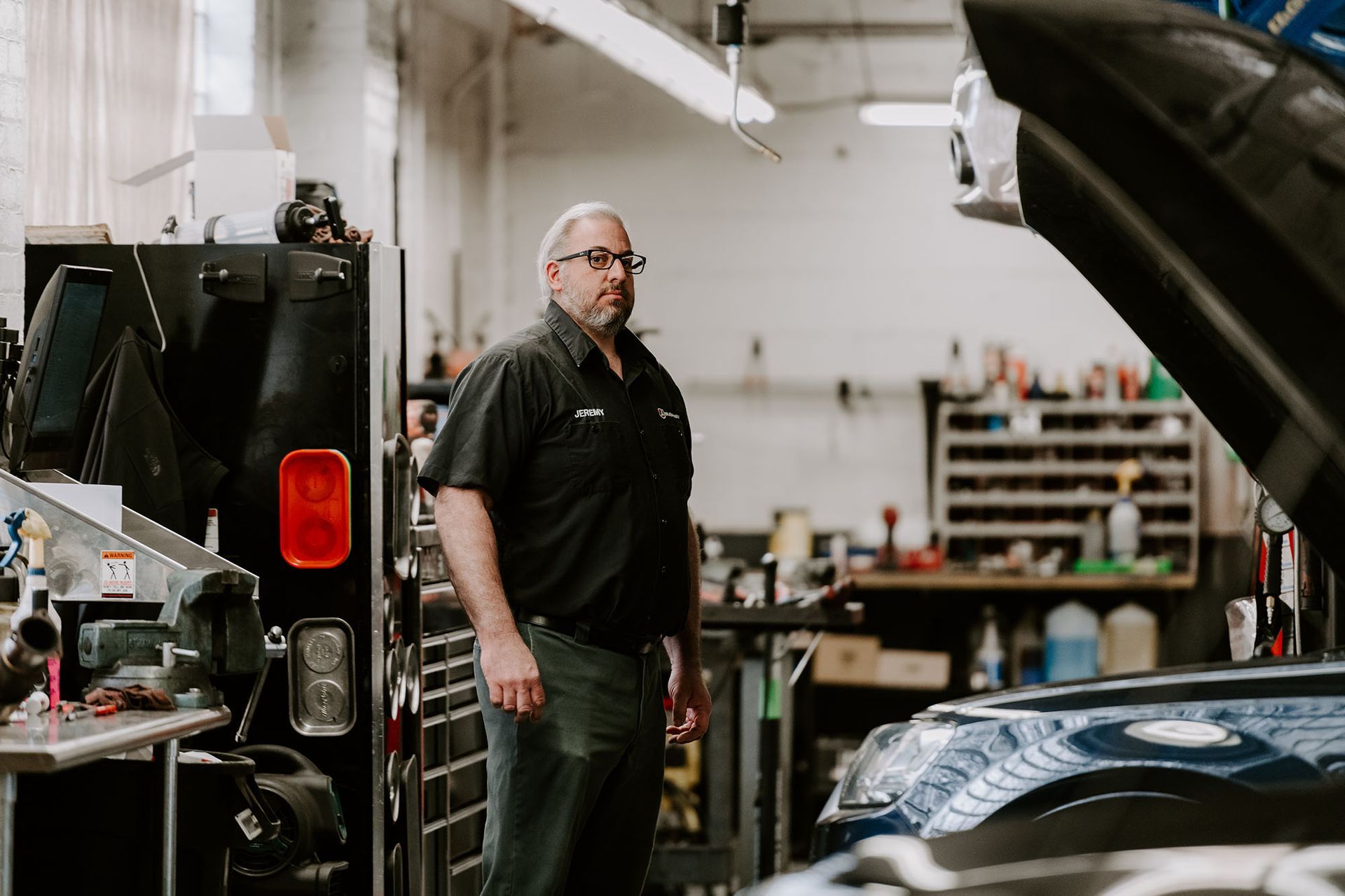 Mechanic standing in an auto repair shop beside a vehicle lift and toolshelves