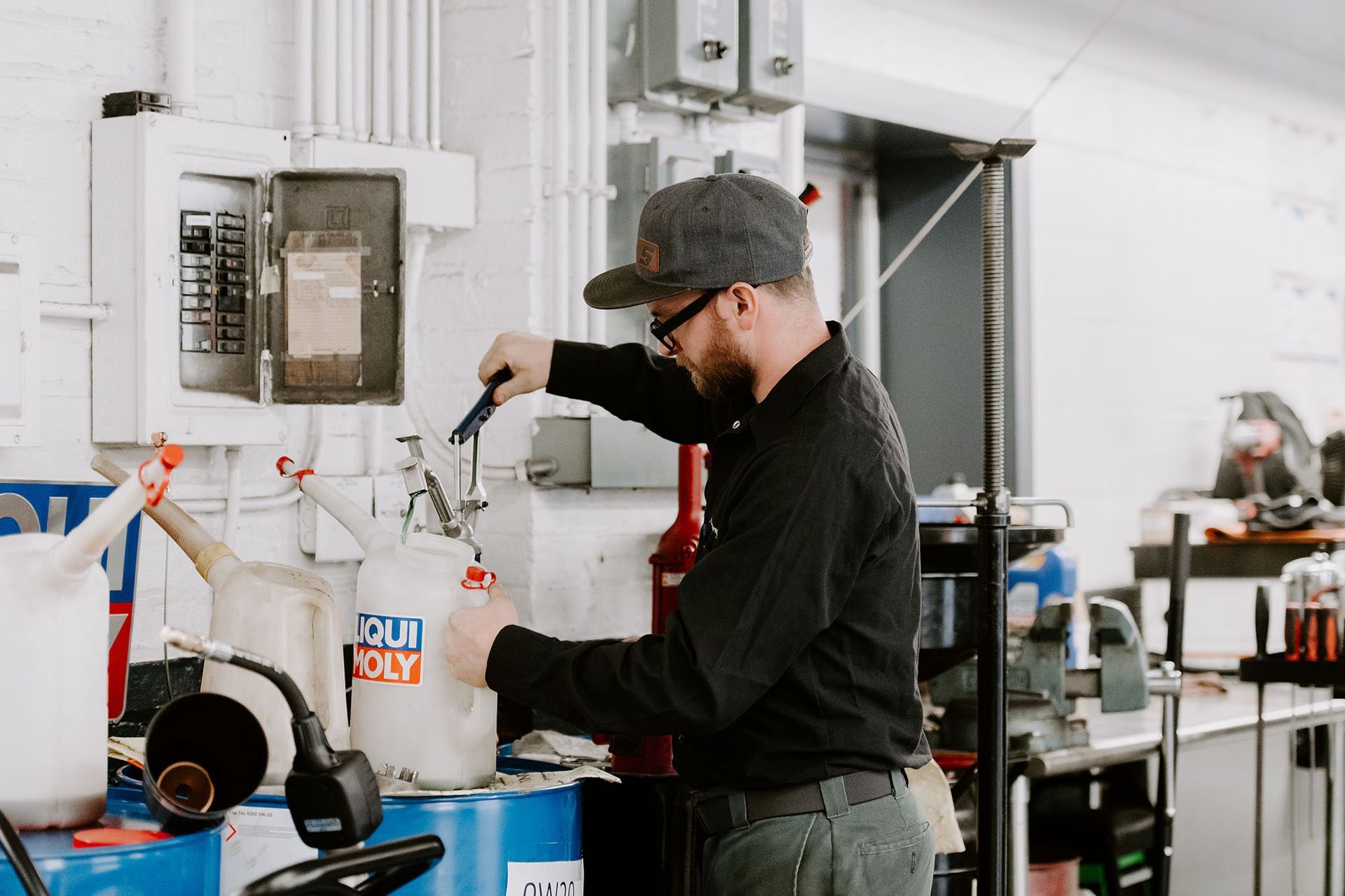 Person operating a spray gun in a workshop beside paint buckets and equipment