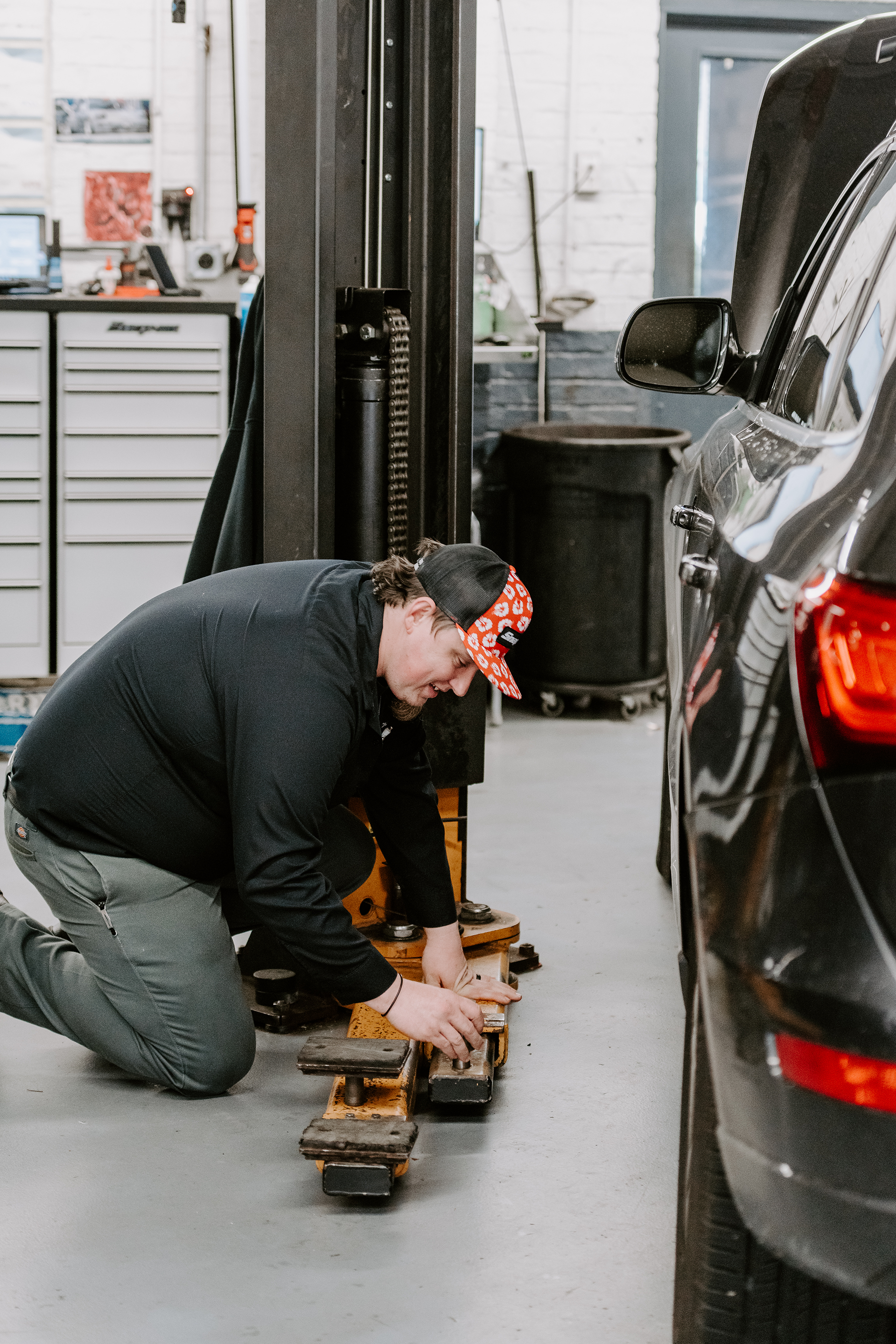 Mechanic crouching beside a black car, working with tools in an auto repair garage