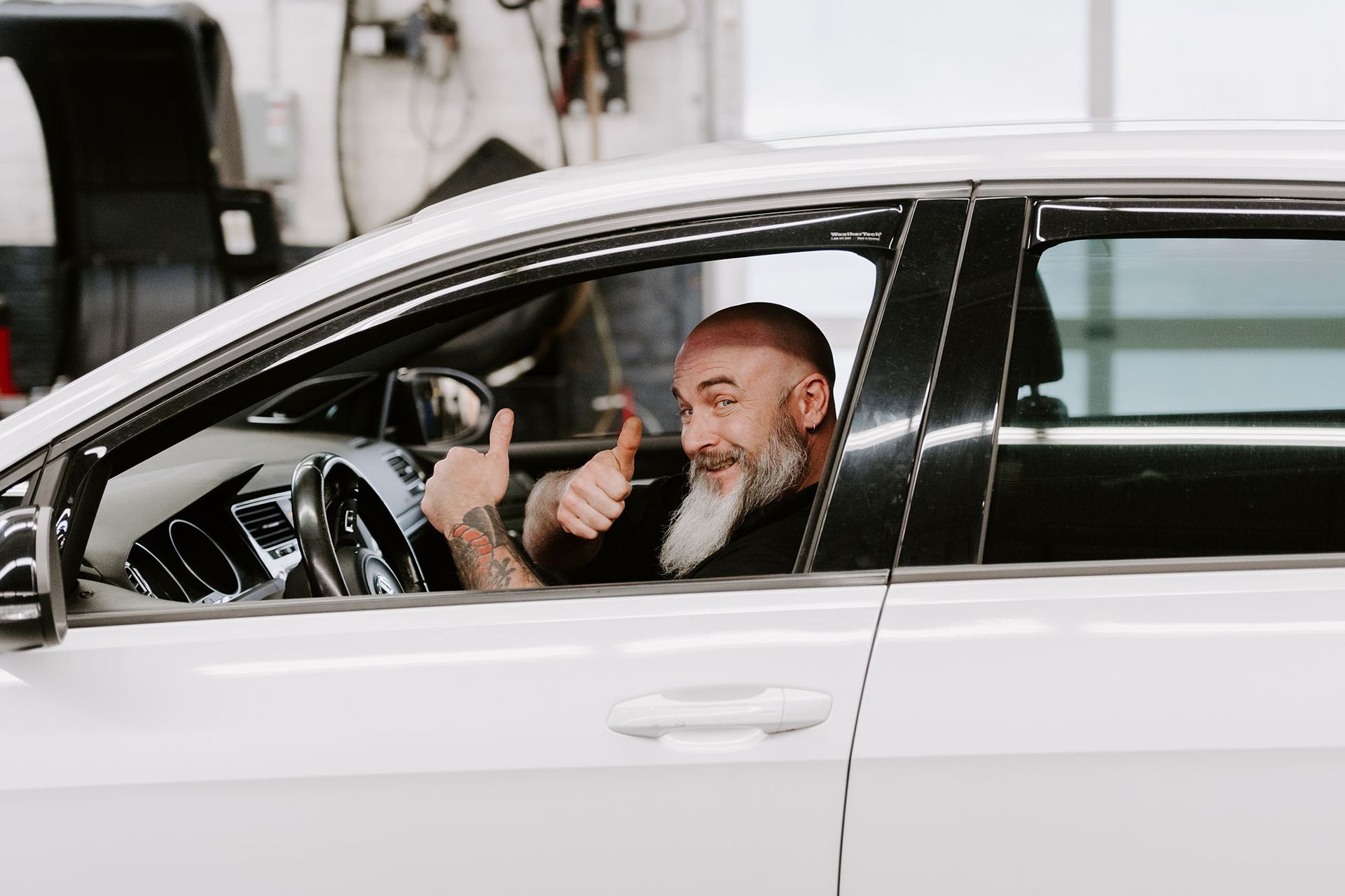 Man smiling and giving a thumbs-up while seated in a white car