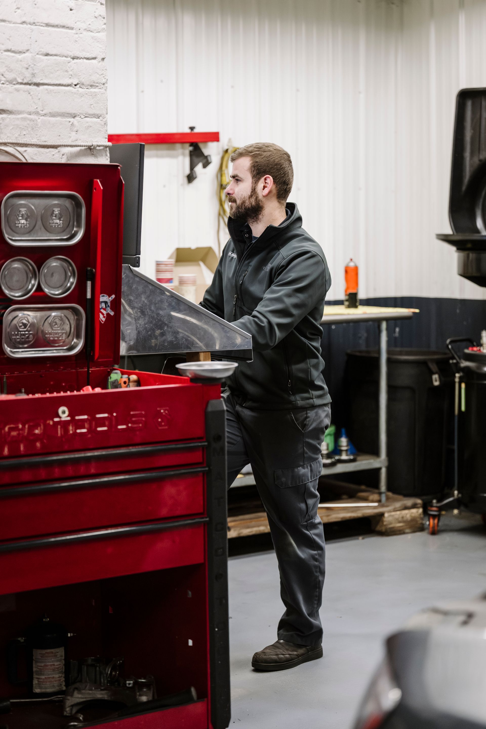 Mechanic working at a red tool cabinet in a workshop, holding a plastic-covered part.