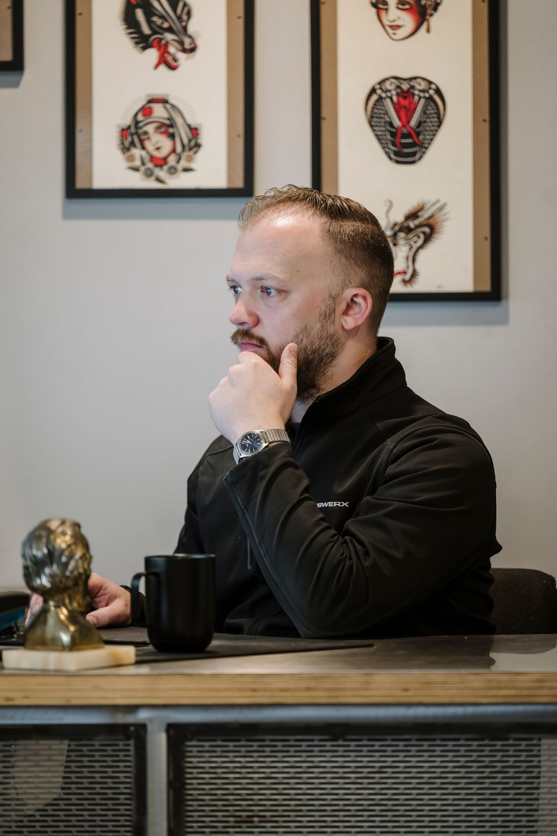 Side-profile of a man sitting at a desk, resting his chin on his hand in a framed-art office space.