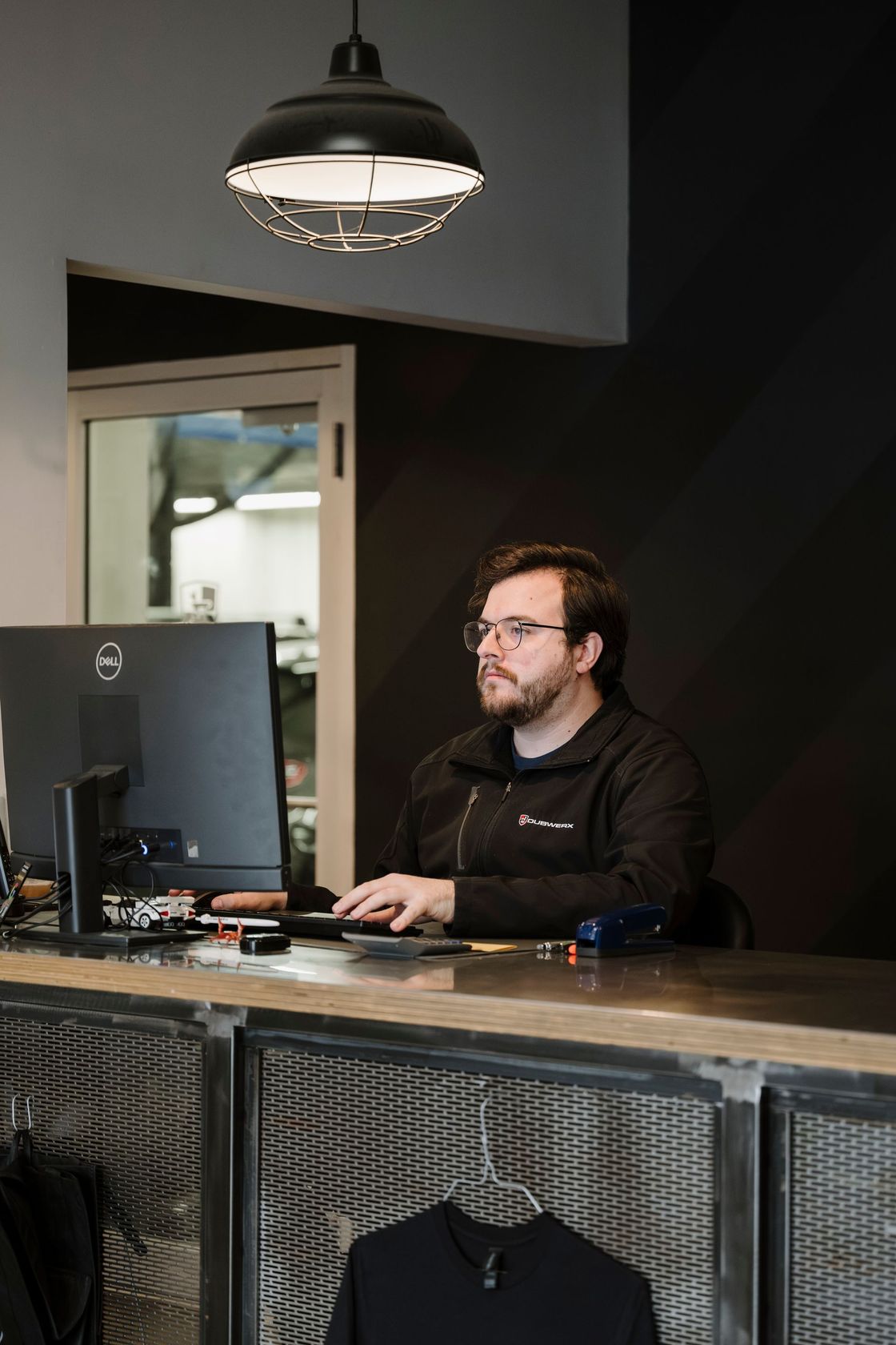 Man working at a computer behind a counter in a dimly lit office or shop