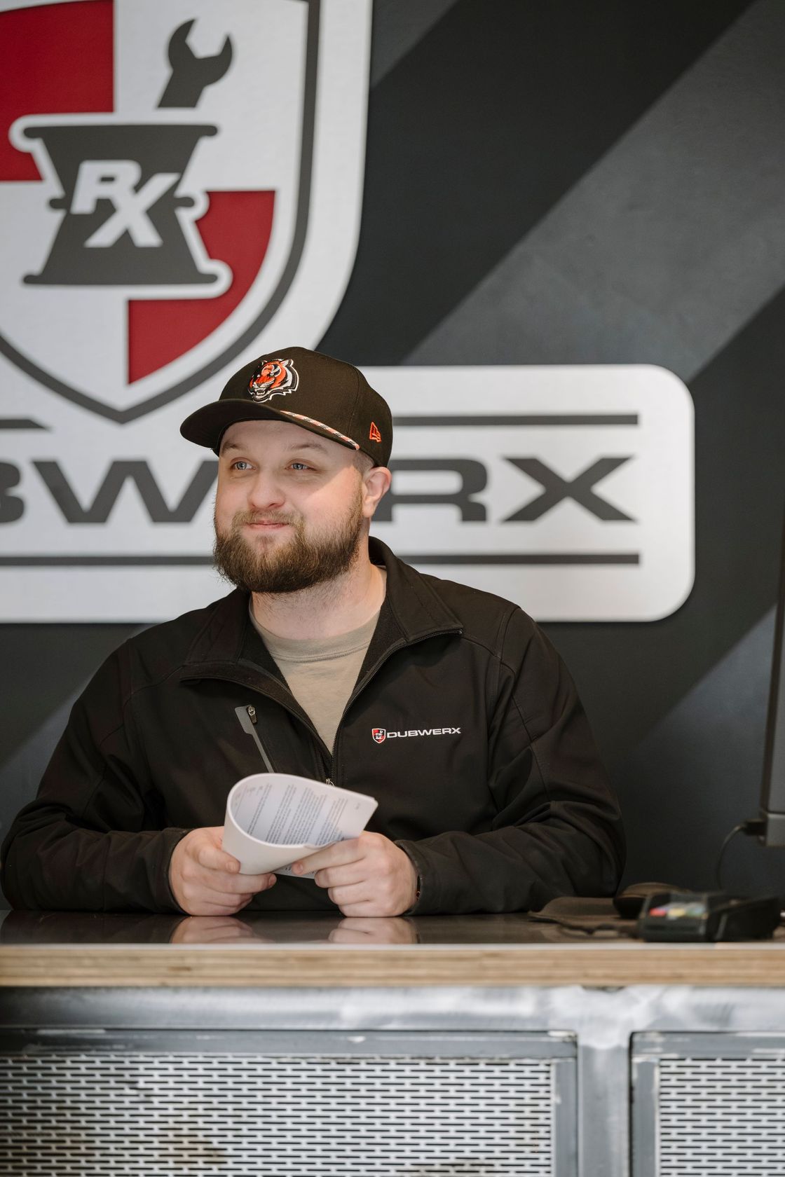 Man behind a counter holding cards, with a BWXR sign on the wall behind him.