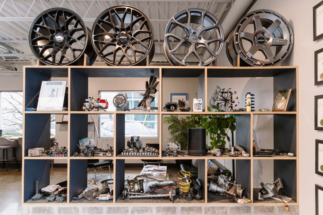 Wall-mounted display of alloy car wheels above a wooden shelving unit with models, plants, and decor pieces