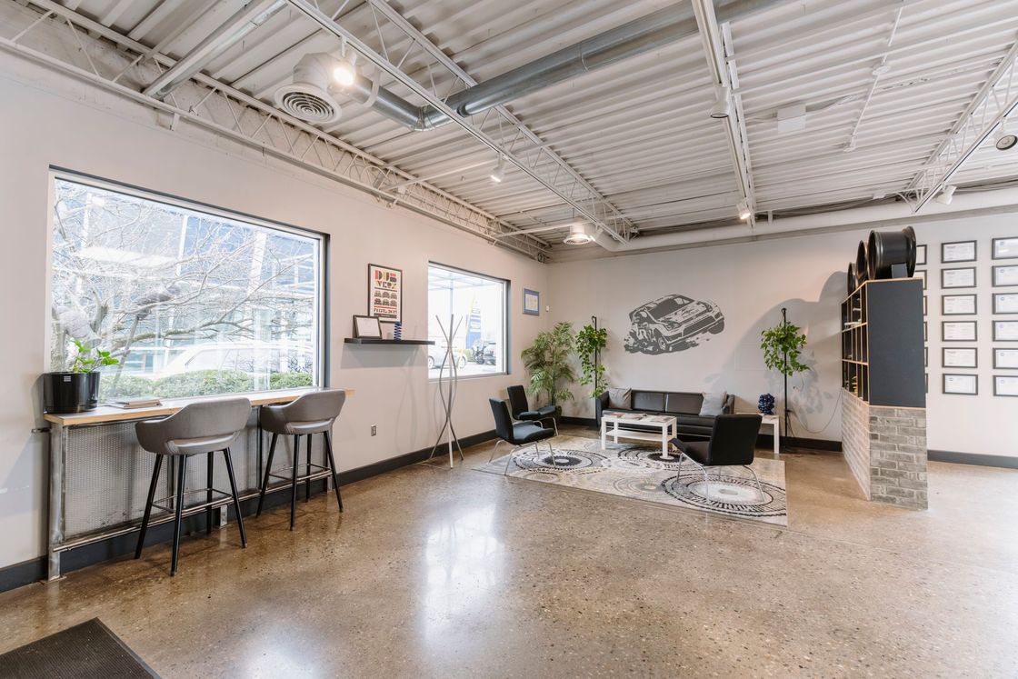 Bright open office lounge with large windows, desk, seating area, plants, and polished concrete floor