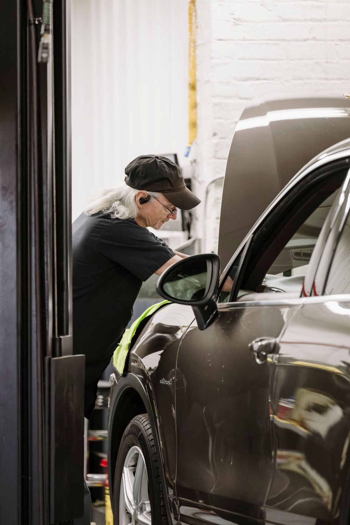Mechanic working on a car inside a garage, leaning into the open driver’s side window.