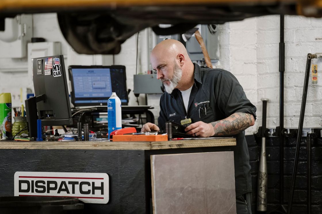 Mechanic working at a dispatch desk with tools and a computer monitor in a garage workshop