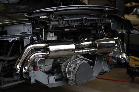 Shiny custom car exhaust system mounted on the rear of a vehicle in a garage