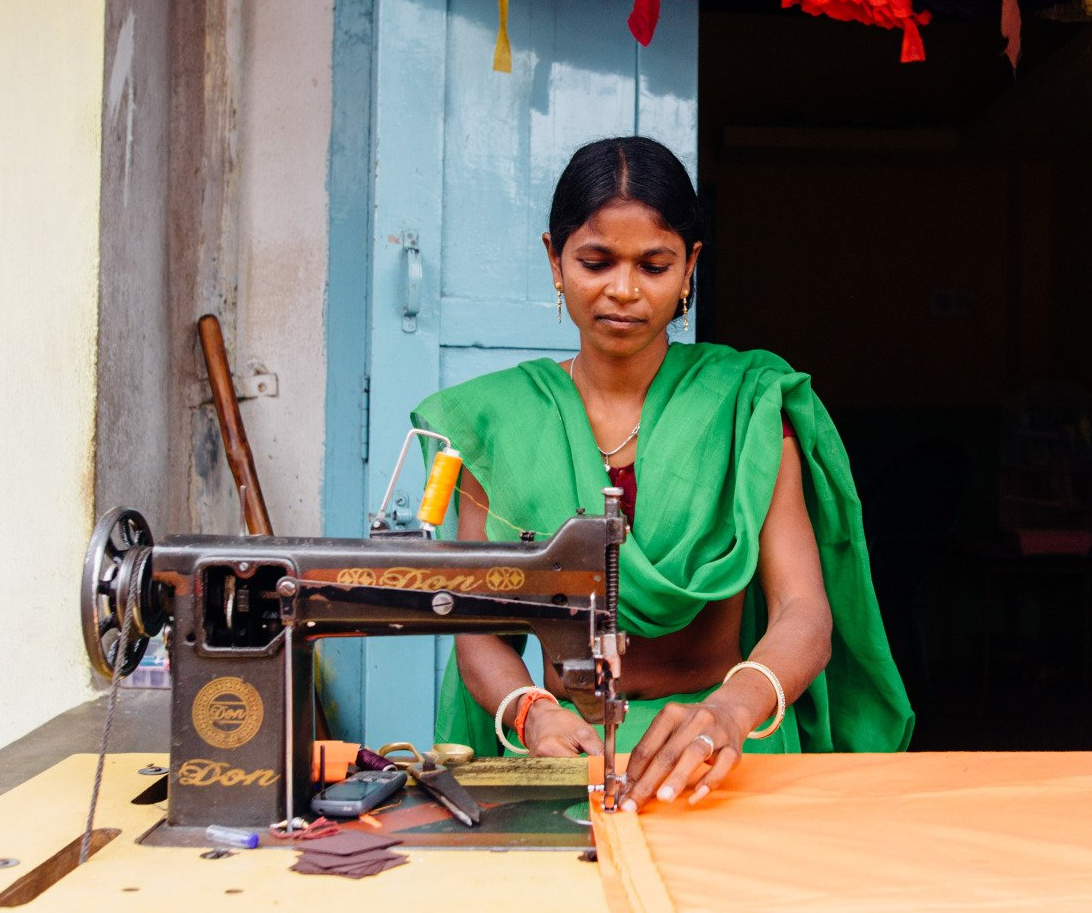 A woman in a green sari is using a singer sewing machine