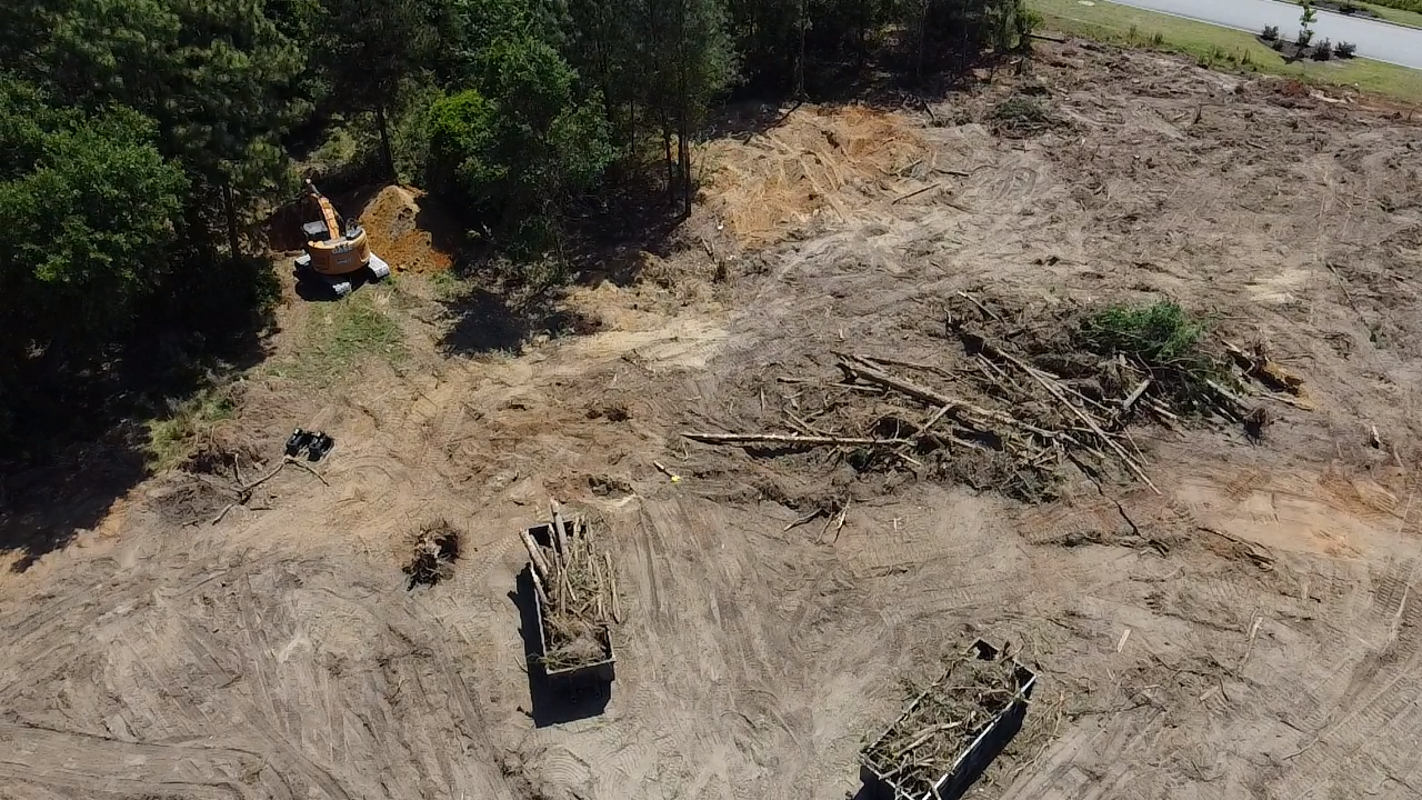Aerial view of a muddy clearing with a tank near trees and another vehicle on bare ground
