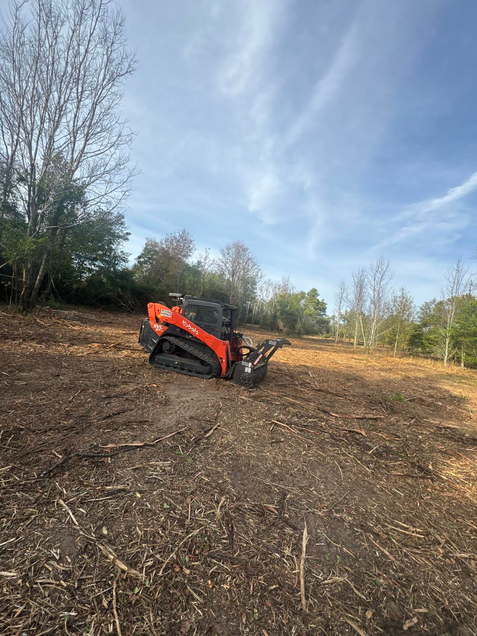Orange excavator on a dirt hillside clearing land under a blue sky