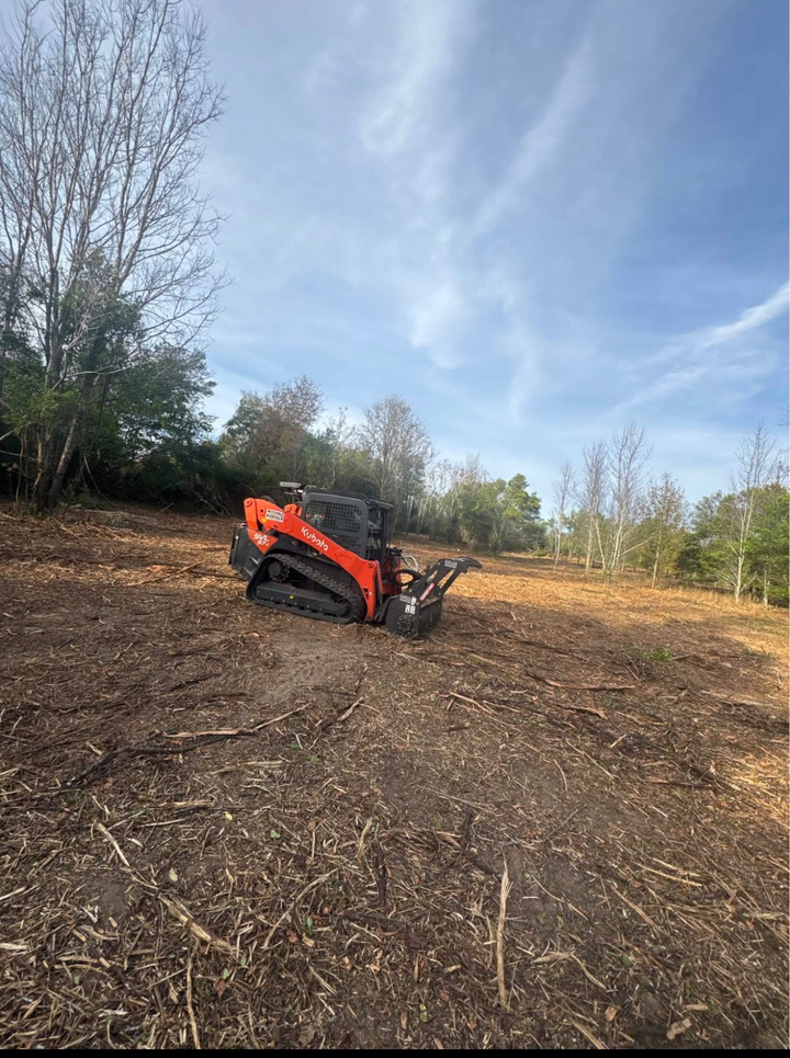 Orange compact tractor in a cleared field with trees and blue sky in the background
