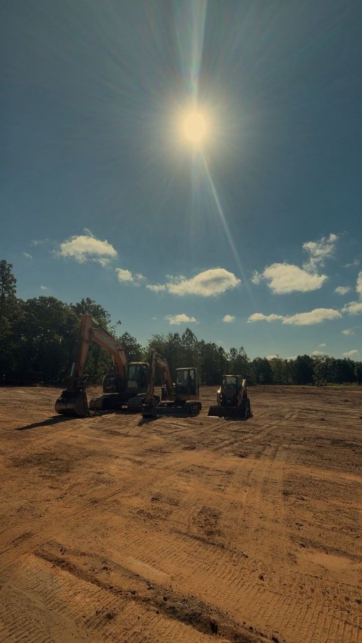 Three off-road vehicles on a dusty dirt lot under a bright sun and blue sky with scattered clouds