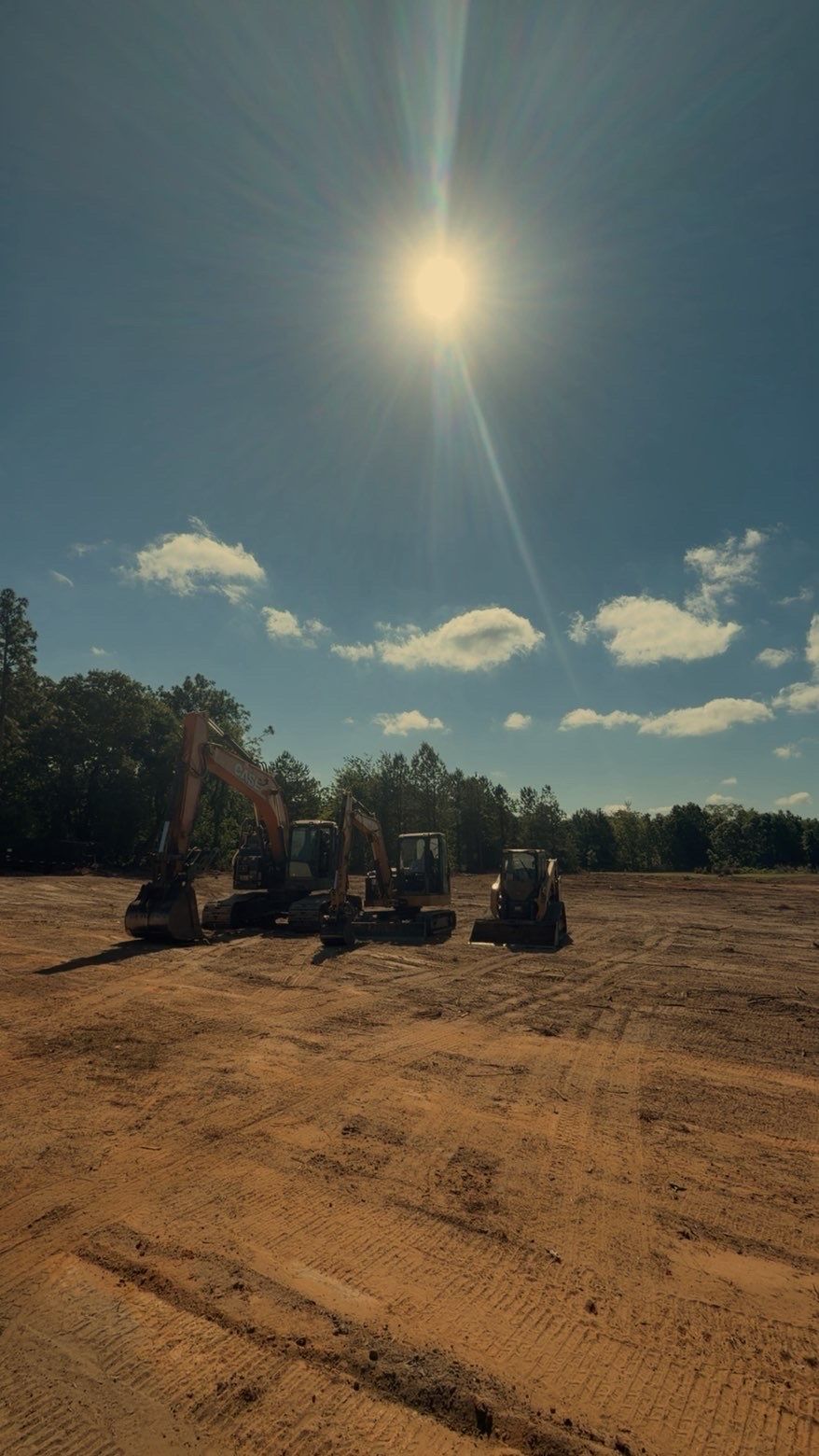 Off-road vehicles parked on a dusty field under a bright sun and blue sky with clouds