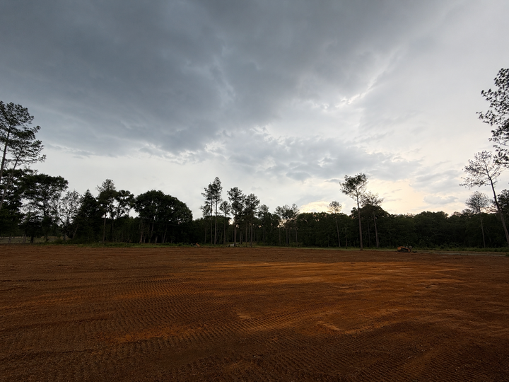 Dark cloudy sky over a barren brown field with a tree line at sunset
