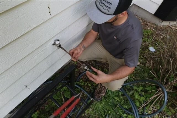 Technician working on an outdoor hose bib beside house siding