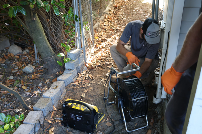 Worker using a cable reel in a narrow outdoor alley beside a building and stone wall