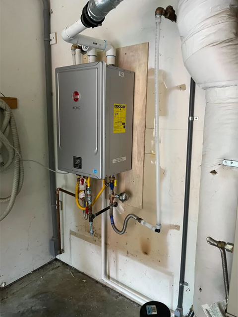 Wall-mounted gray tankless water heater with pipes and valves in a utility room