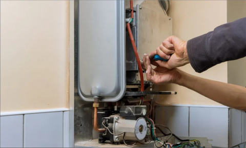 Technician adjusting pipes and wiring on a wall-mounted boiler unit in a utility room