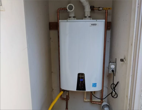 Wall-mounted tankless water heater with plumbing and vent connections in a utility closet